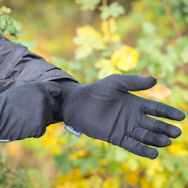 Lifestyle shot outdoors of a person wearing a pair of Extremities Silk Liner Gloves in black