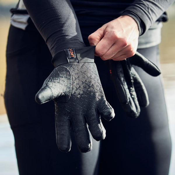 Lifestyle photograph of a person putting on Extremities Waterproof Insulated Sticky Power Liner Touchscreen Gloves outside near water