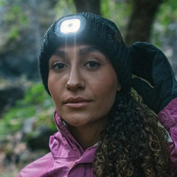 Lifestyle image of a women wearing a Sealskinz Heydon waterproof knitted hat with the LED light on whilst outdoors in a forest