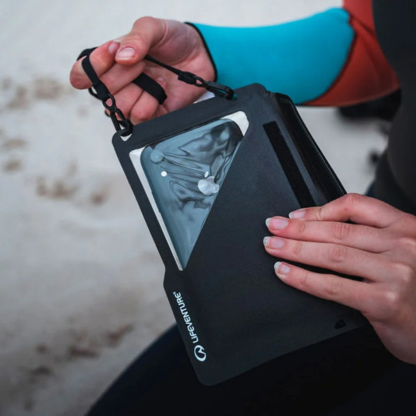 Woman in a wetsuit holding a Lifeventure Waterproof Phone Pouch Plus with her mobile inside whilst on the beach